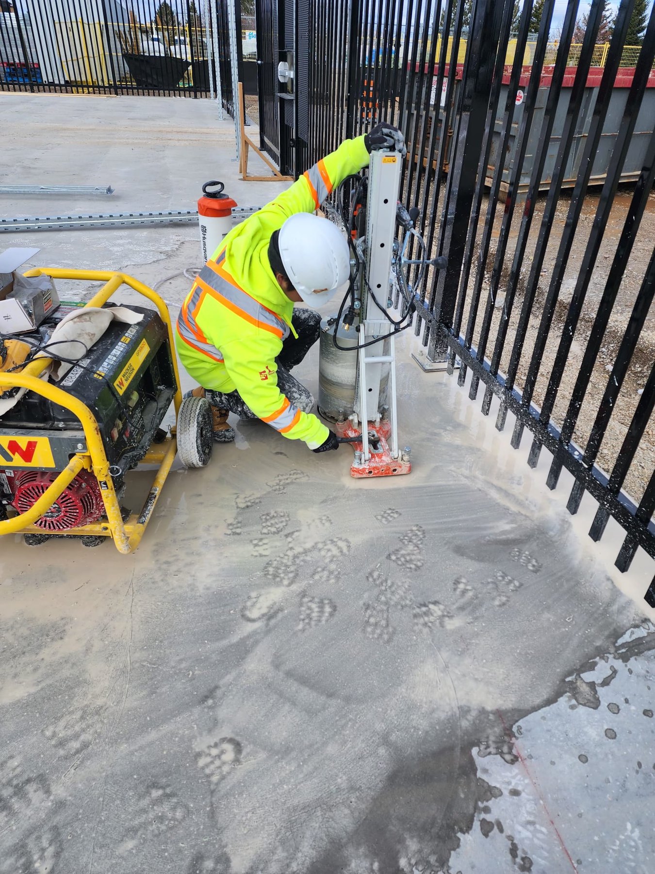 Worker in high-visibility PPE operating a core drill beside the Canadian Tire Collingwood fence