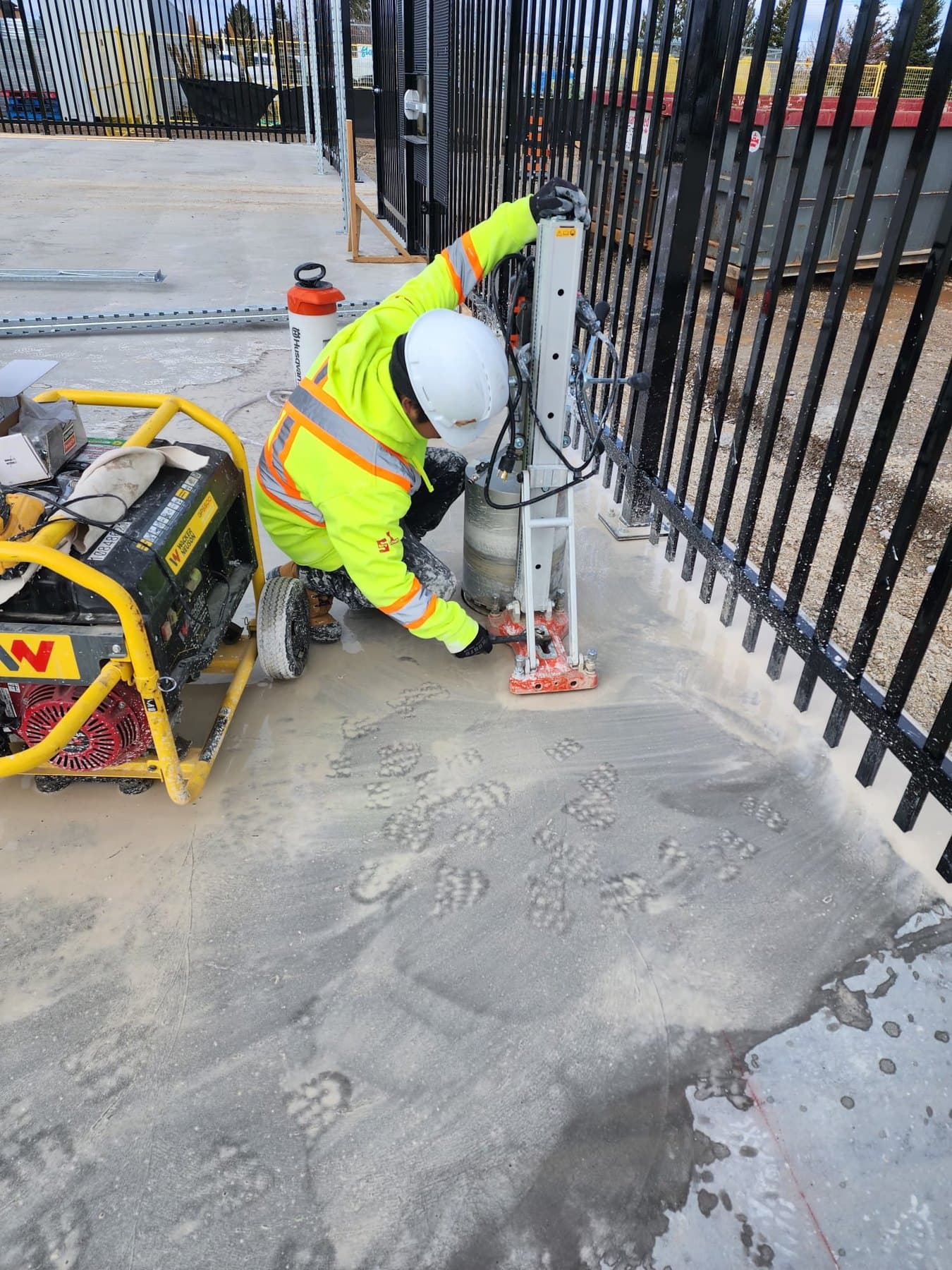 Worker in high-visibility PPE operating a core drill beside the Canadian Tire Collingwood fence
